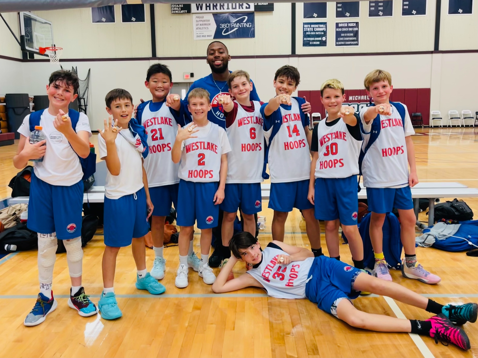 Westlake Hoops Select team posing with championship rings inside the Warriors gym.
