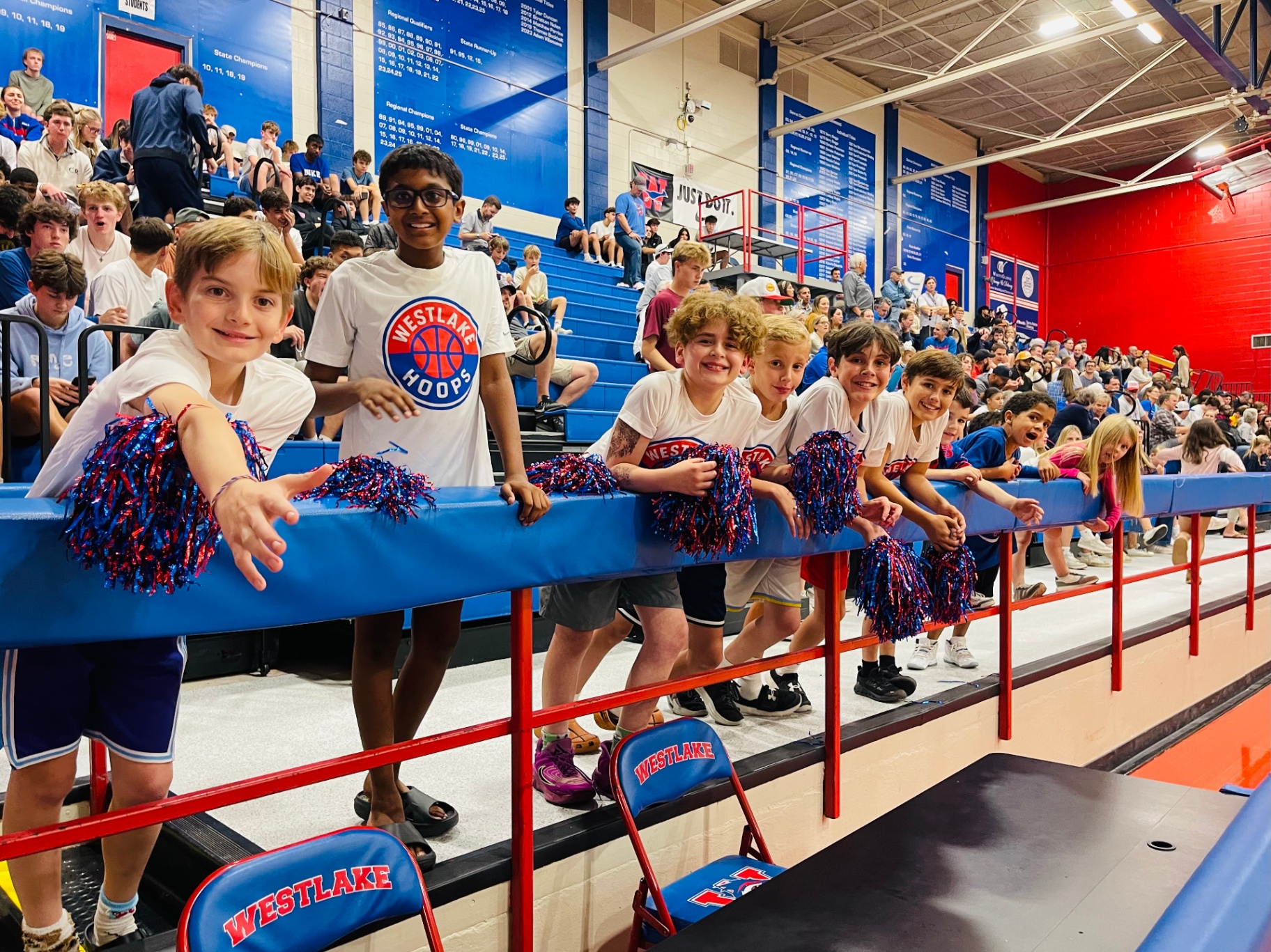 Westlake Hoops players lined up along the rail cheering on the Chaps varsity team.