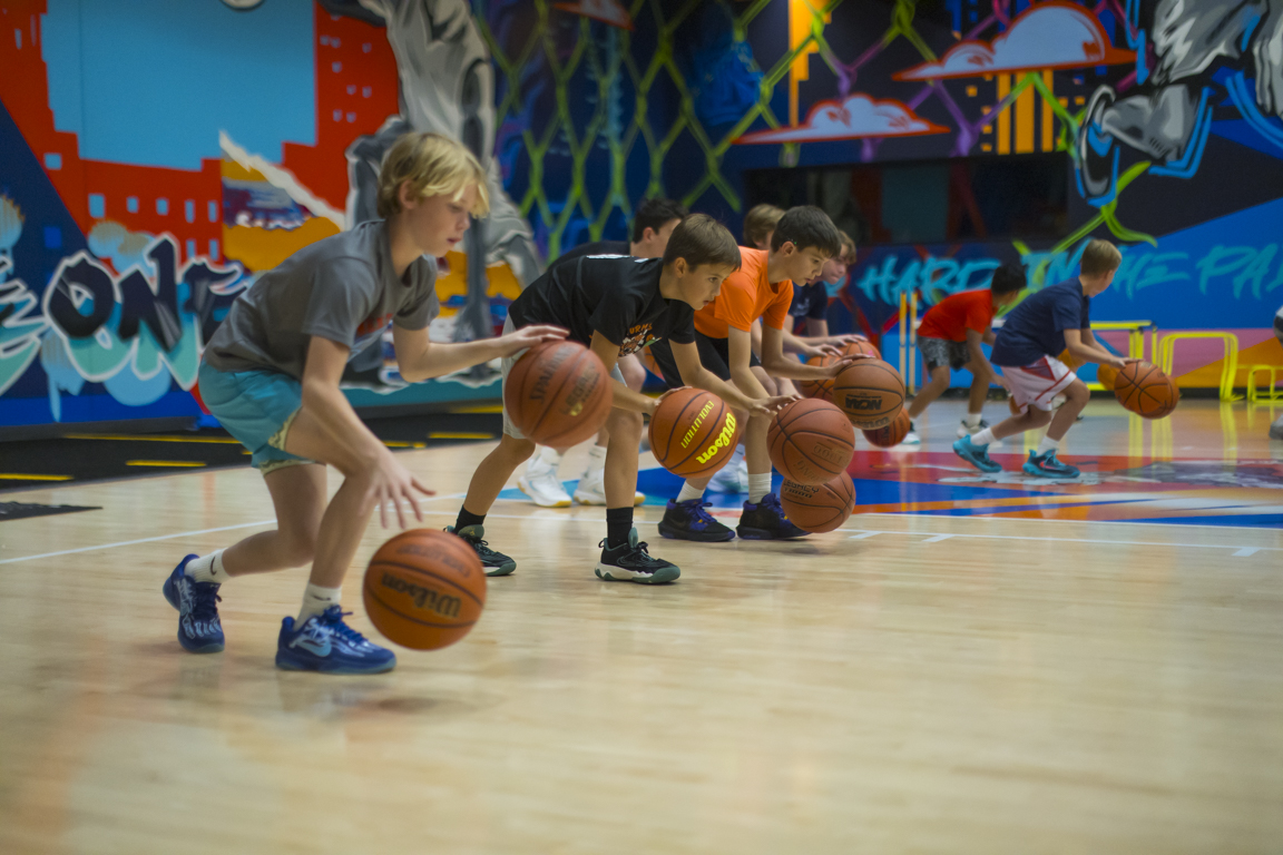 Line of athletes running a low-stance dribbling drill across the court.